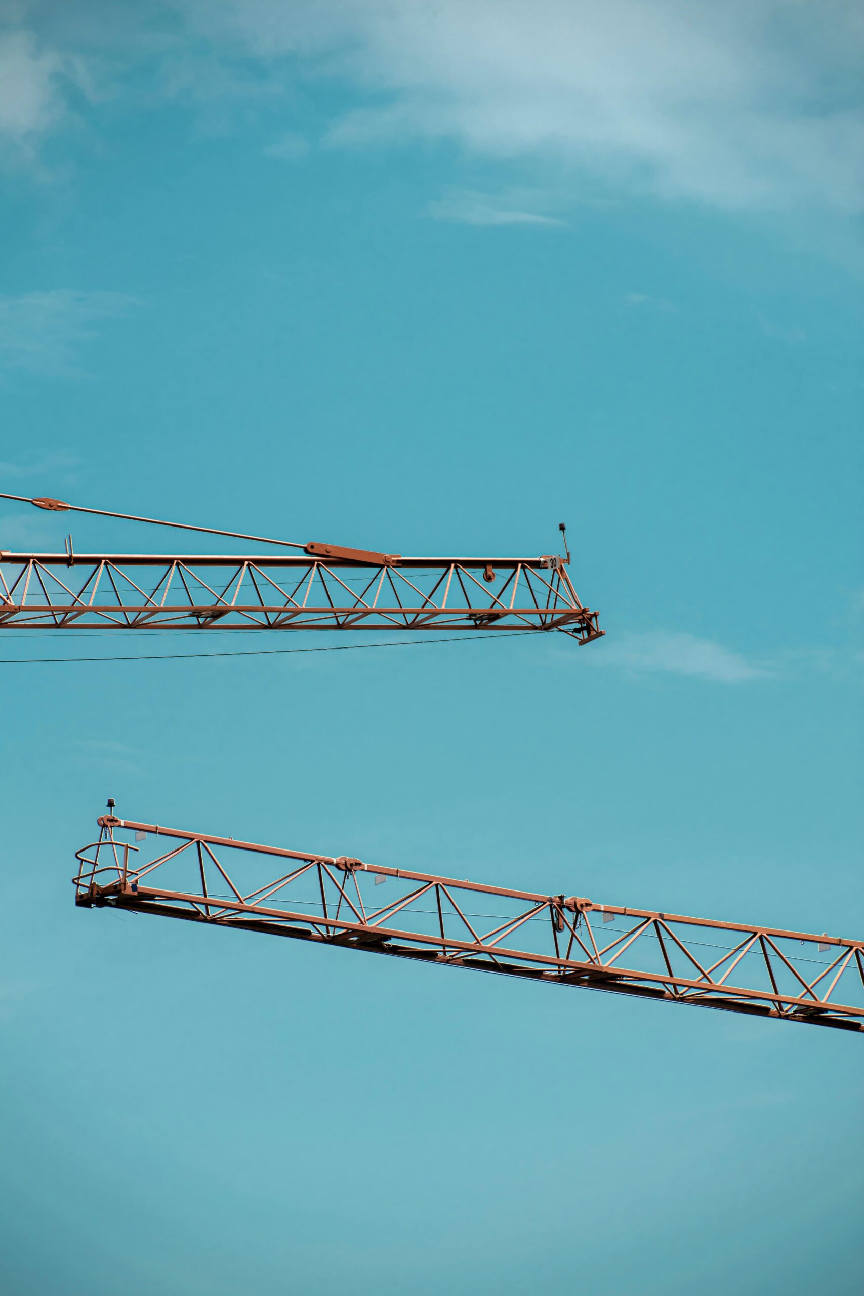 A minimalist view of construction cranes set against a clear blue sky, showcasing modern industrial design.